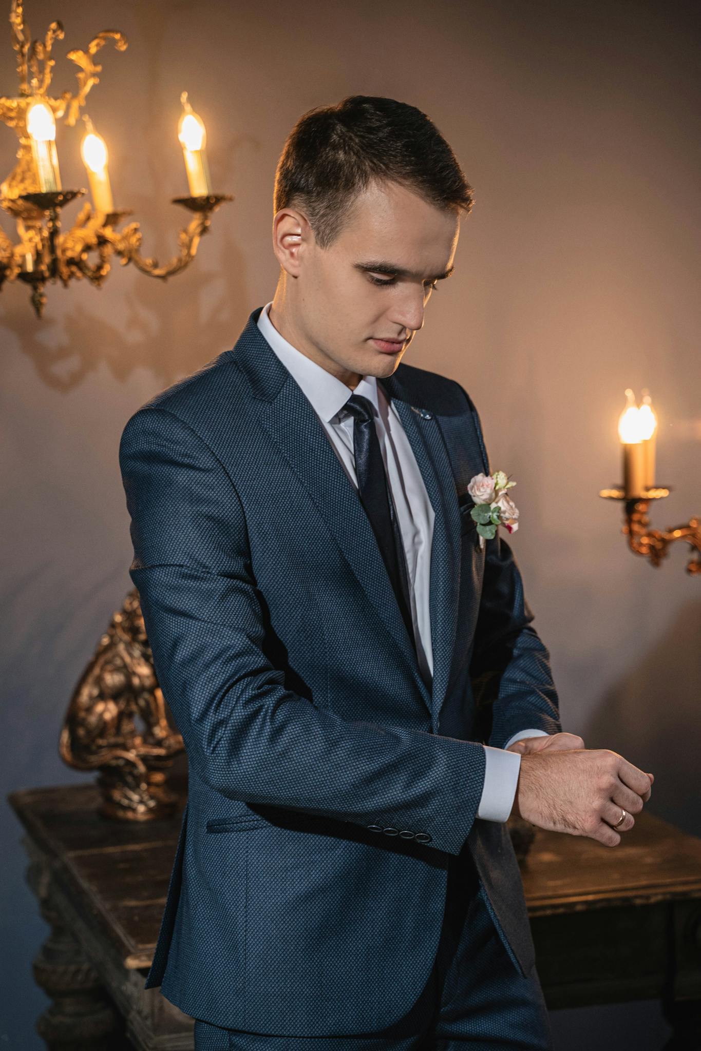 Elegant groom adjusting suit in candlelit room, creating a classic wedding vibe.